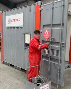 David in his red work overall with safety glasses and gloves, painting a Kaefer container in grey